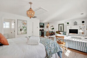 Ein modernes, helles Schlafzimmer mit einem großen Bett, einem Schreibtisch und einem Fernseher.