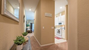 A hallway leading to a kitchen with beige walls, a wooden bench with potted plants, and a 'HAPPINESS' sign on the wall.