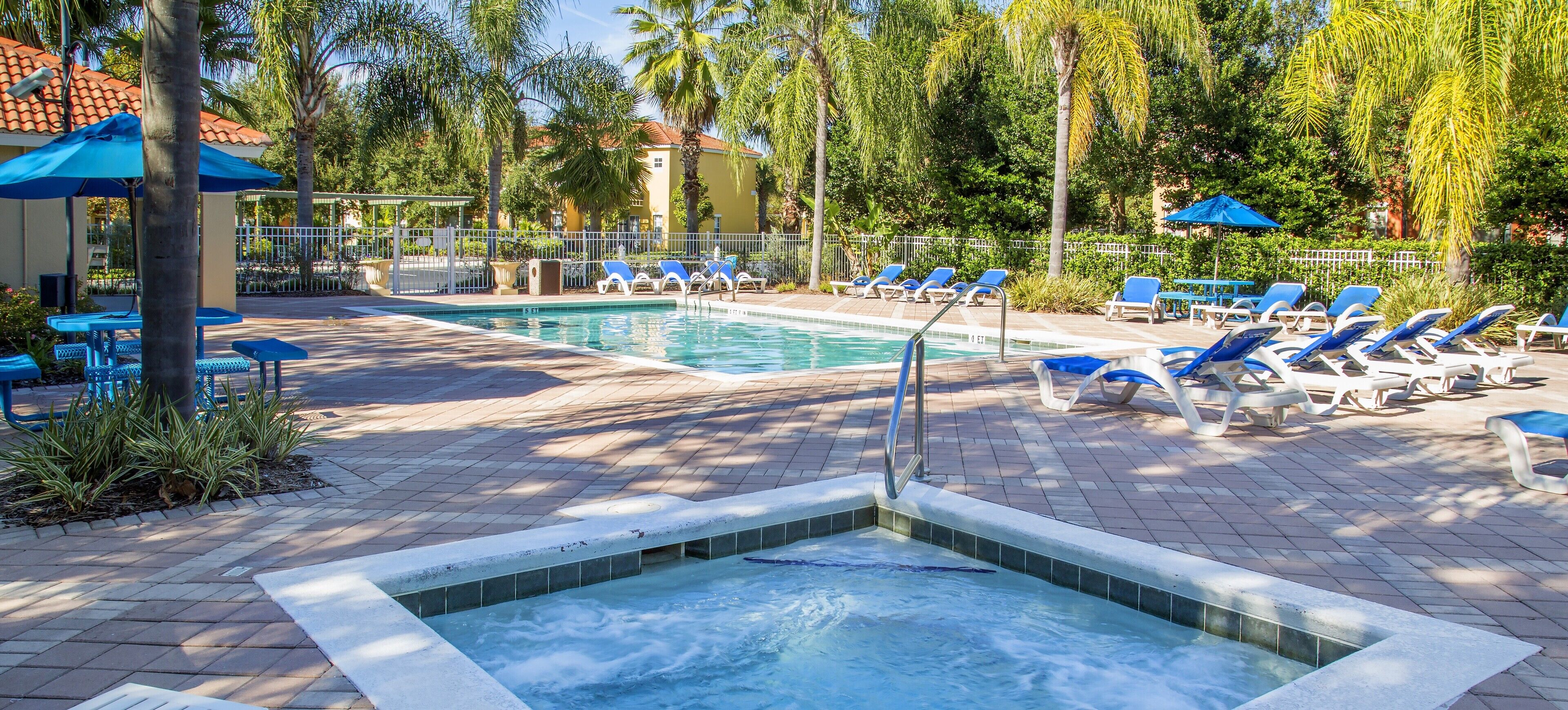A pool area with lounge chairs, a hot tub, and a tiled deck.