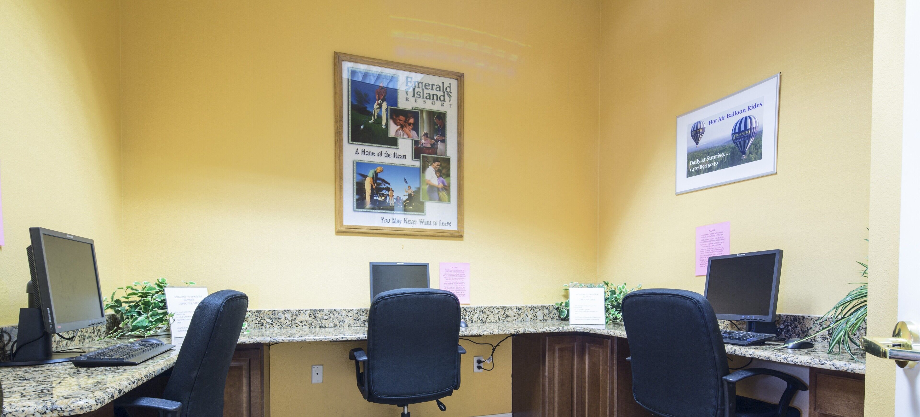 A reception area with two computer workstations, a framed photo collage on the wall, and a potted plant.