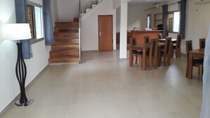 Een ruime woonkamer met een houten trap, een eettafel met stoelen en een moderne keuken op de achtergrond.