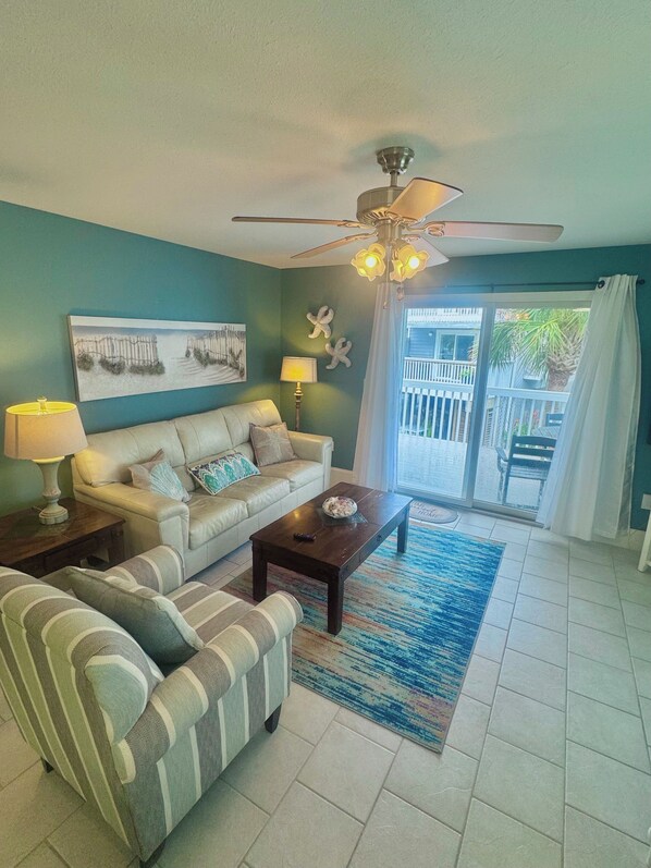 A living room with a sofa, armchair, coffee table, and a ceiling fan.