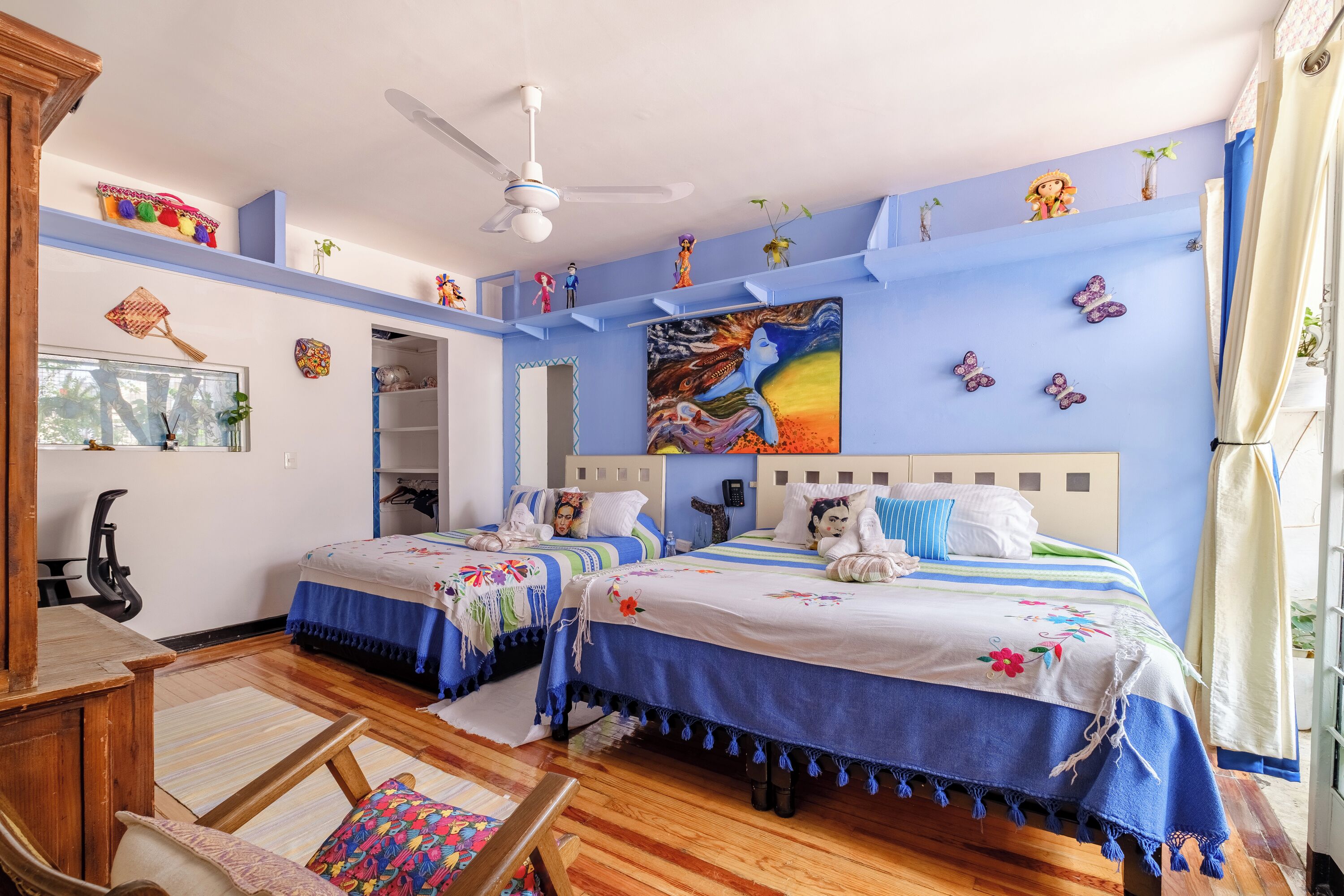 Un dormitorio con dos camas, un ventilador de techo y un cuadro grande en la pared.