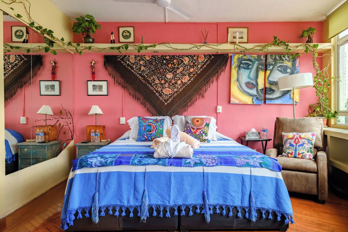 A bedroom with a bed, pillows, a chair, a nightstand, and a mirror.