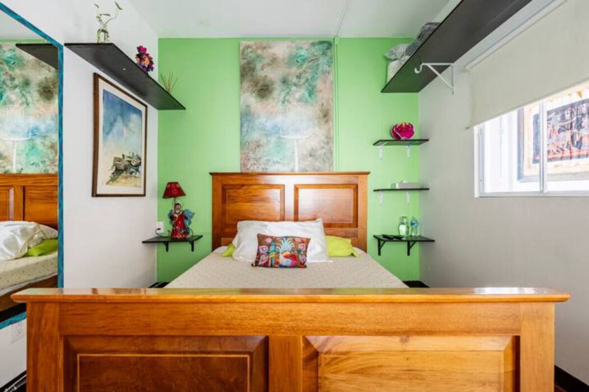 A bedroom with a wooden bed, green walls, and artwork. There are two bedside tables with lamps and decorative items.