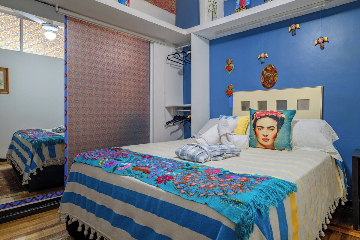 A bedroom with a bed, a nightstand, a mirror, and a window.