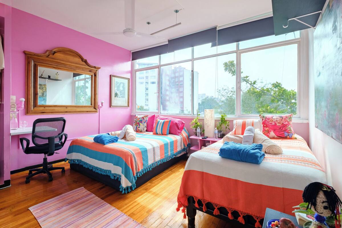 A brightly colored bedroom with two beds, a desk, and a chair.