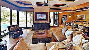 A spacious living room with a large sofa, a coffee table, and a television. There is a dining area with a table and chairs.