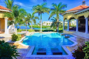 A swimming pool with a clear blue water, surrounded by palm trees and a building with a red roof. - Tierra Verde - St. Petersburg Waterfront Mansion Estate - Pool - Boat Dock (Tierra Verde)