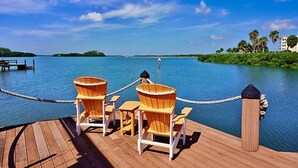 A wooden deck with two Adirondack chairs and a rope barrier overlooking a calm body of water.