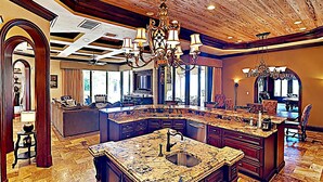 A spacious kitchen with a large island, a chandelier, and a view to the dining area.