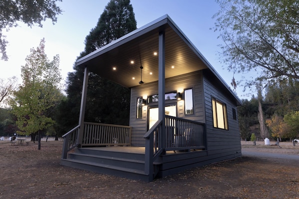 Step up to this cozy cabin's entrance, flanked by two windows, and enjoy the natural surroundings.