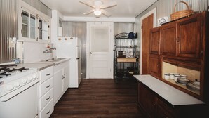 Cocina compacta con gabinetes blancos, estufa y microondas. Cuenta con ventilador de techo y puerta que da a otra habitación.