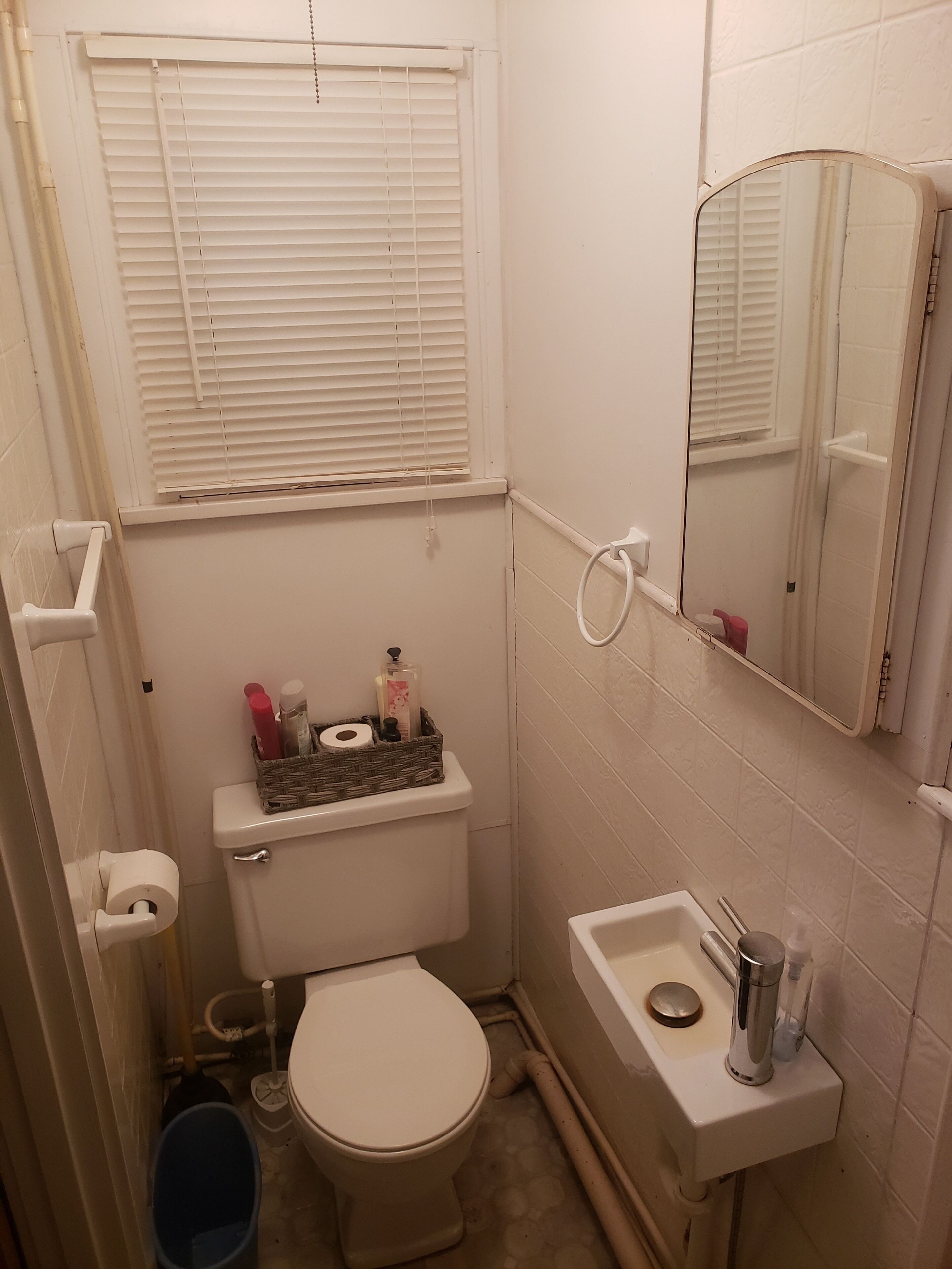 A small bathroom with a toilet, sink, and window with blinds.