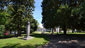 Ein Park mit einem Denkmal, Bäumen und einem Gebäude im Hintergrund.