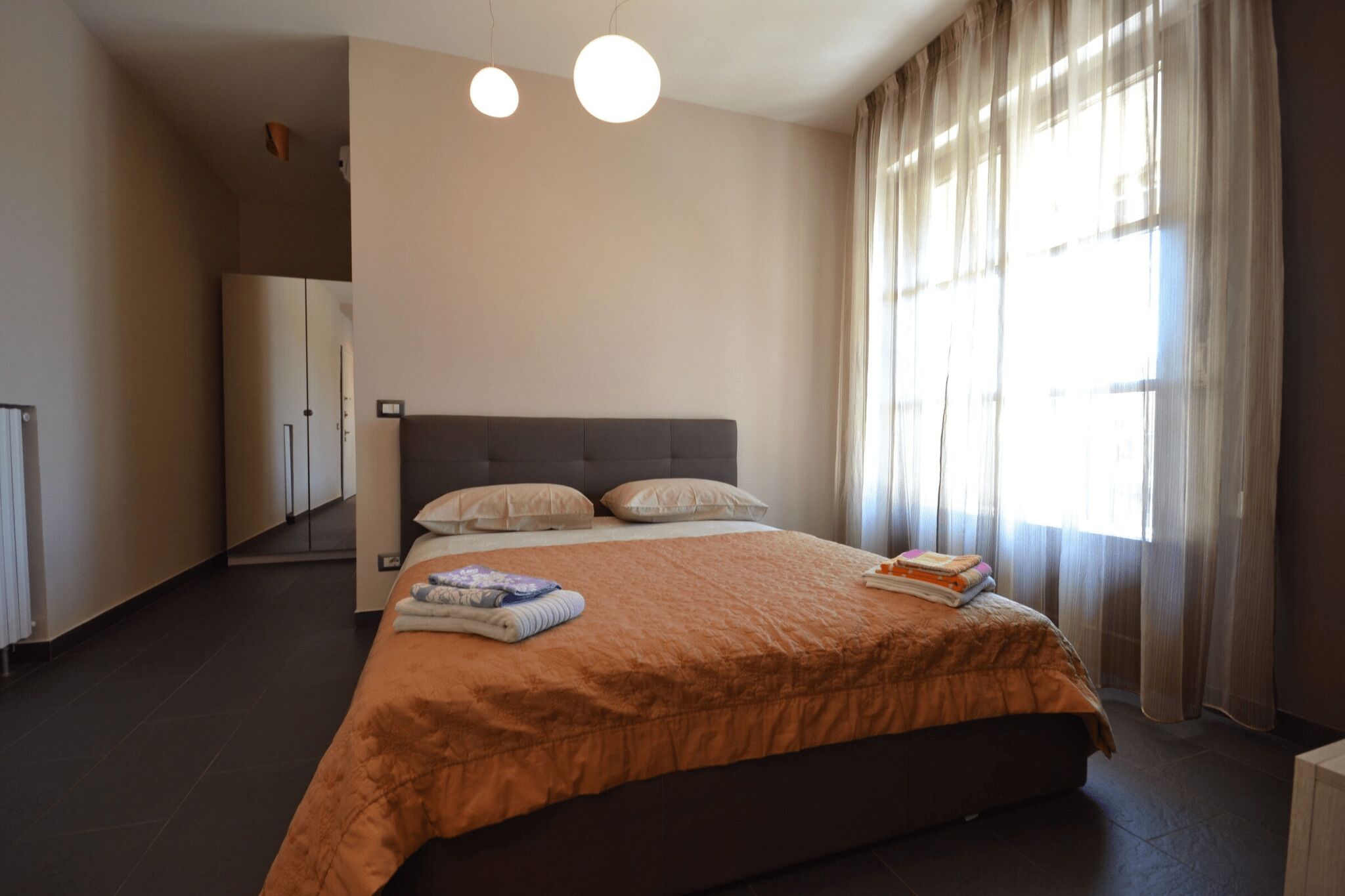 A bedroom with a large bed, a wardrobe, and a window with curtains.