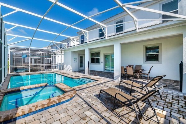 A pool area with a glass-enclosed patio, lounge chairs, and a dining table.