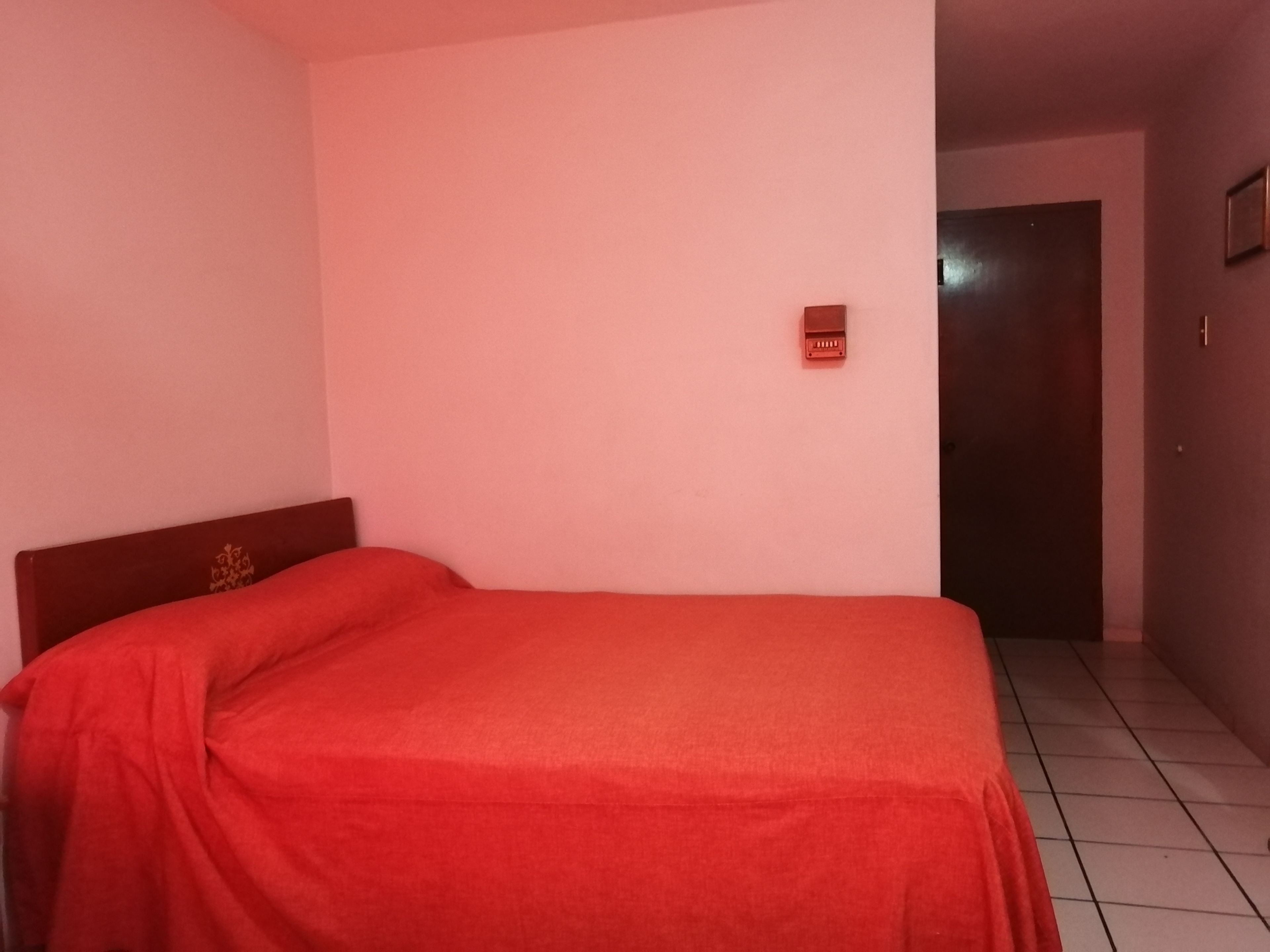 Quarto com uma cama de solteiro, uma porta e um interruptor de luz fixado na parede.