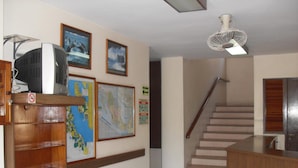 Un hall d’entrée avec un escalier, un comptoir d’accueil en bois, un téléviseur et des tableaux encadrés accrochés au mur.
