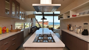 A modern kitchen with a central island, a stove, and a view of the ocean. - Casas Punta Costanera (Pichilemu)