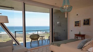 A bedroom with a large sliding glass door leading to a balcony overlooking the ocean. - Casas Punta Costanera (Pichilemu)