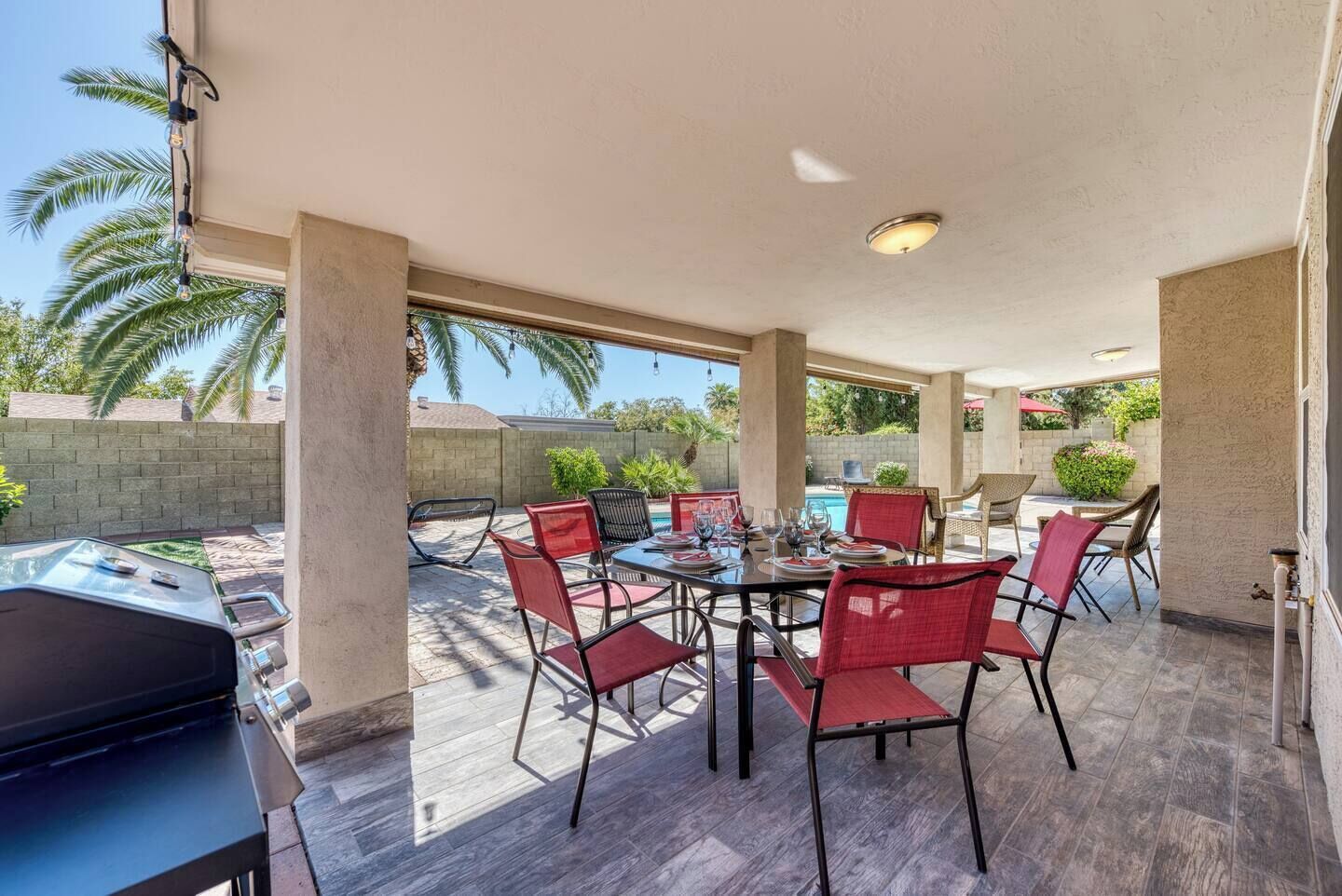 An outdoor patio with a round table, red chairs, and a barbecue grill.