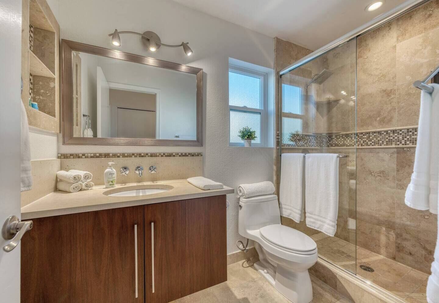 A modern bathroom with a large mirror, a sink, a toilet, and a glass-enclosed shower area.