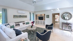 Un salón amplio con un sofá blanco, sillones azules, una mesa de centro y un televisor.