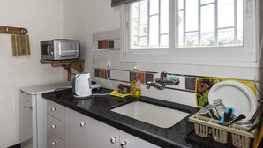 Una cocina compacta con un lavamanos, un microondas, una tetera y una ventana con persianas.