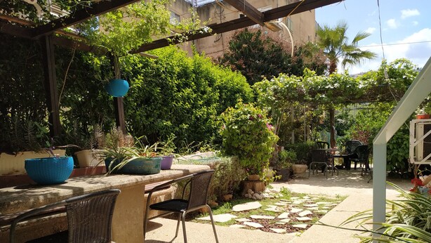 Un patio al aire libre con una mesa y sillas de piedra, rodeado de plantas en macetas y follaje.