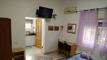 Un dormitorio con una cama, un escritorio con silla, un televisor y una ventana con cortinas.