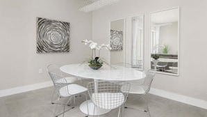 A modern dining area with a round table, wire mesh chairs, and abstract wall art. - 5 min to Disney Precious Villa (Kissimmee)