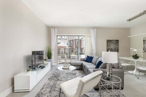 Een moderne woonkamer met een flatscreen televisie, een bank, een salontafel en een eethoek met een tafel en stoelen.