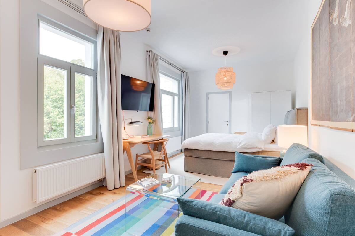 A modern bedroom with a bed, a desk, a TV, and a sofa.