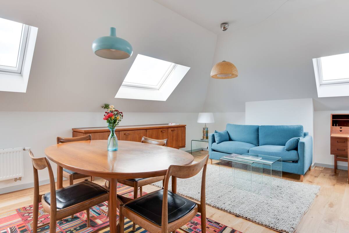 A modern loft apartment with a dining area, a sofa, and a kitchenette.