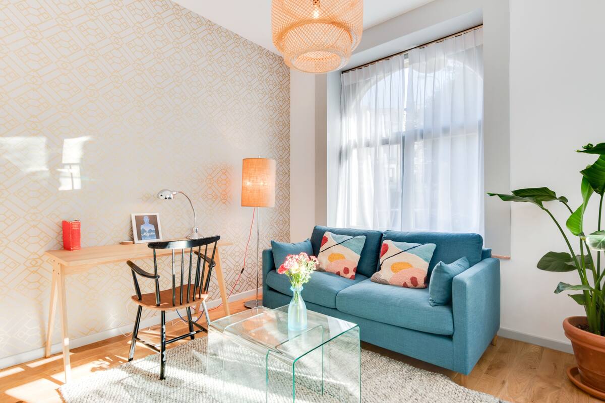 A modern living room with a blue sofa, a glass coffee table, a wooden desk, and a large potted plant.