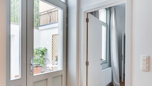 A hallway with a door leading to a balcony with a potted plant and a view of a wooden fence. - Europea Newton Boutique Hotel Residences (Brussels)