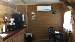 A wooden cabin interior with a kitchenette, a dining area with a table and chairs, an air conditioning unit, and a mounted deer head. - Our cabins are located on the crystal clear water of Spring Creek. (Mertzon)