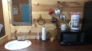 A wooden cabin interior with a sink, mirror, coffee maker, and a microwave. - Our cabins are located on the crystal clear water of Spring Creek. (Mertzon)