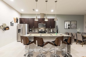A modern kitchen with dark wood cabinets, stainless steel appliances, a central island with bar stools, and pendant lighting.
