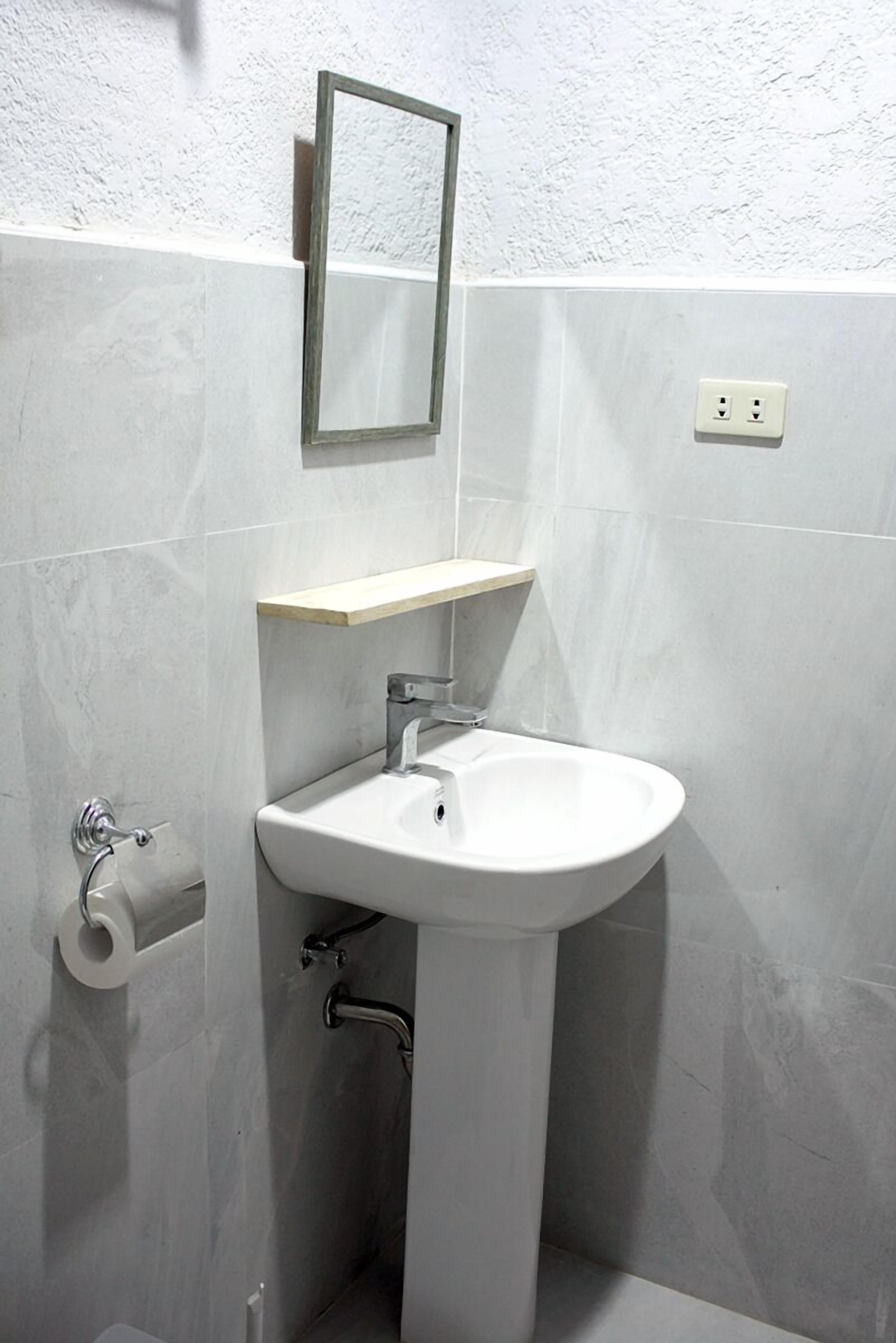A bathroom with a white sink, a mirror, and a toilet paper holder.