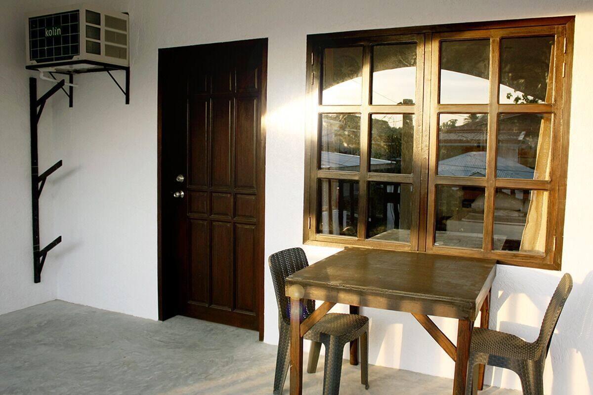 A room with a wooden door, a window with multiple panes, a table with two chairs, and a wall-mounted air conditioning unit.