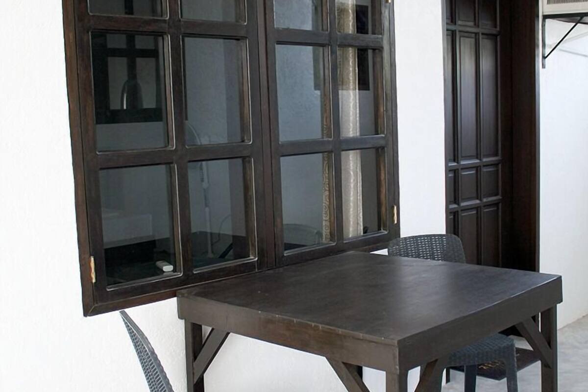 A room with a dark wooden table and chairs, a large window with multiple panes, and a white wall.