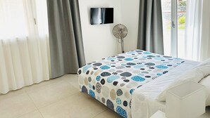 Un dormitorio con cama, televisor, ventilador y vistas al exterior a través de una puerta corrediza.
