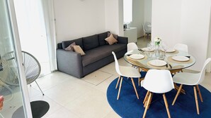 Una sala de estar moderna con un sofá gris, sillas blancas, una mesa de comedor de vidrio y un tapete azul.