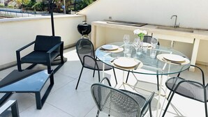 Un patio al aire libre con una mesa redonda de vidrio dispuesta para comer, rodeada de sillas de metal.