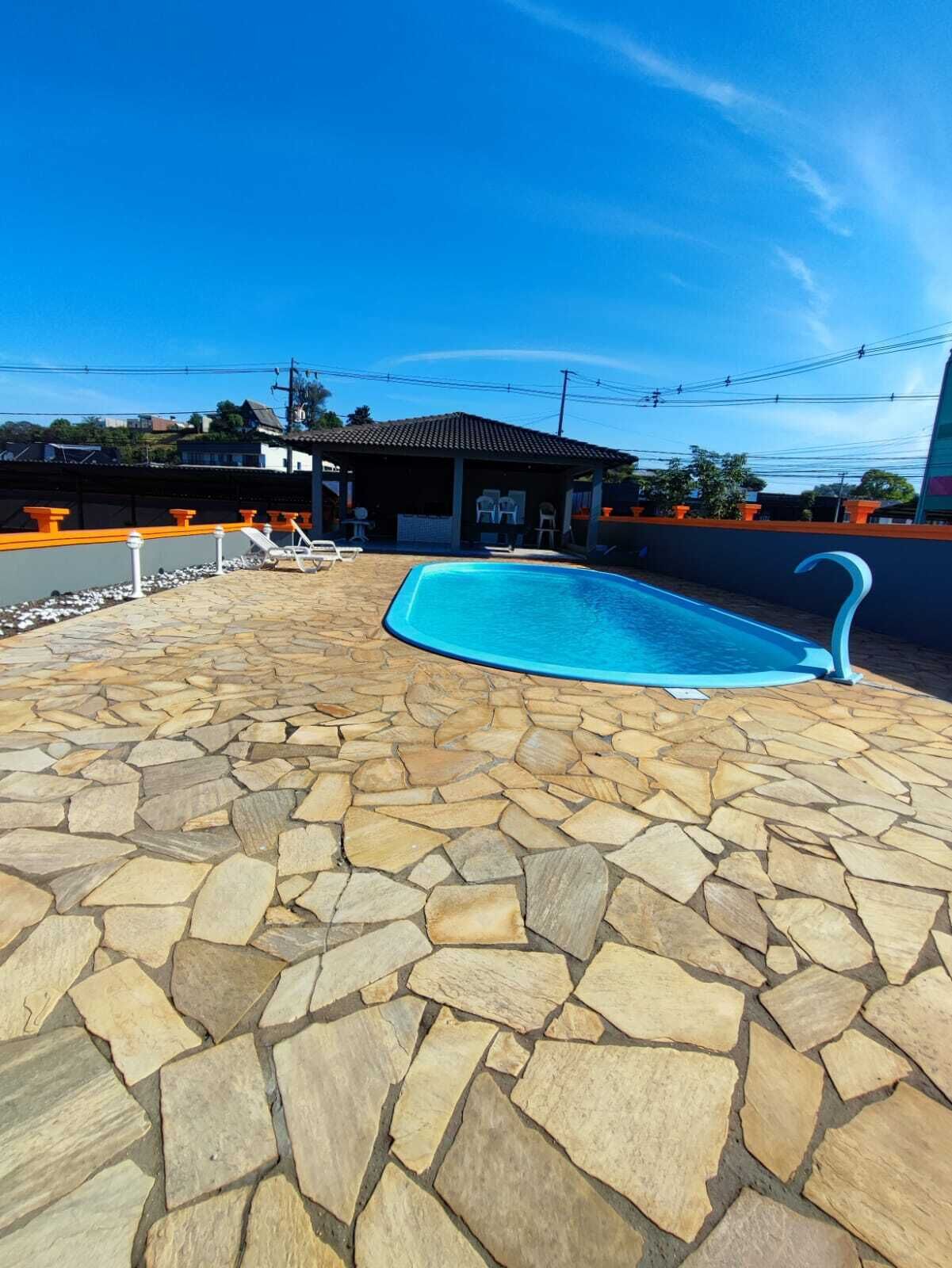 A swimming pool with a stone patio, a covered seating area, and a view of the surrounding neighborhood.