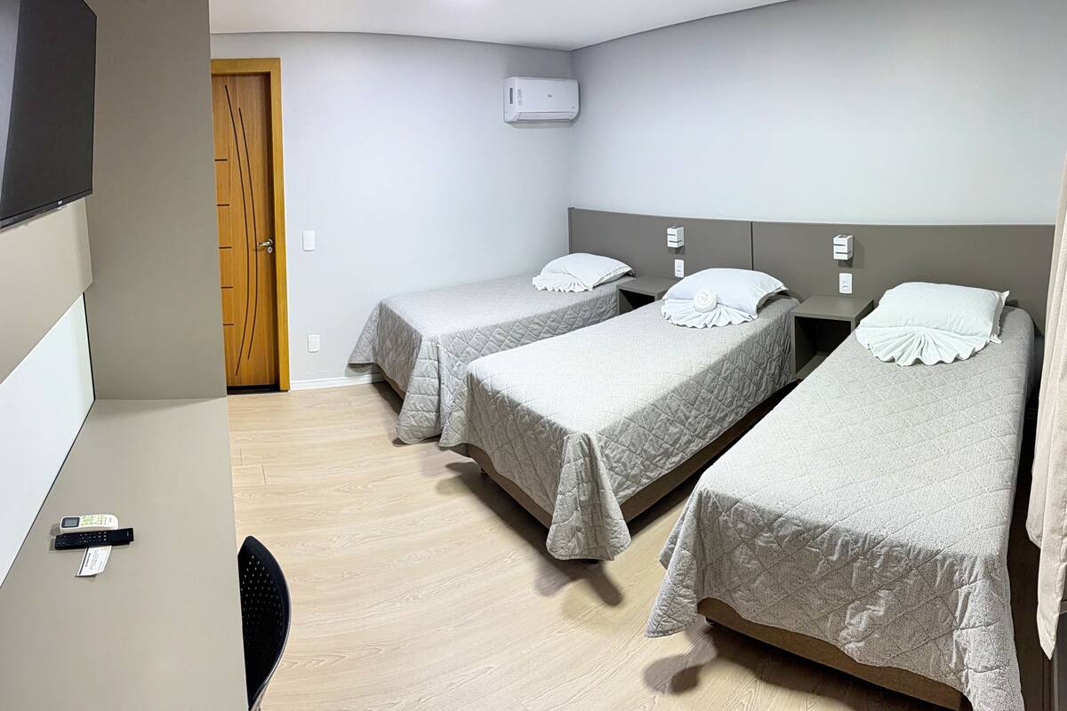 Ein Hotelzimmer mit zwei Einzelbetten, einem an der Wand befestigten Fernseher, einer Holztür und einer Klimaanlage.