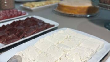 Una mesa de buffet con diversos alimentos, incluyendo queso blanco, carne roja y un pastel.