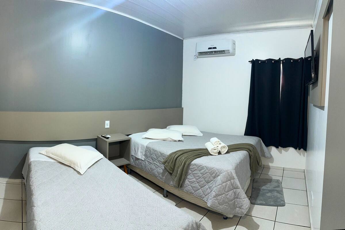Ein Hotelzimmer mit zwei Betten, einem Schreibtisch, einem Sessel, einer Klimaanlage und einem an der Wand befestigten Fernseher.